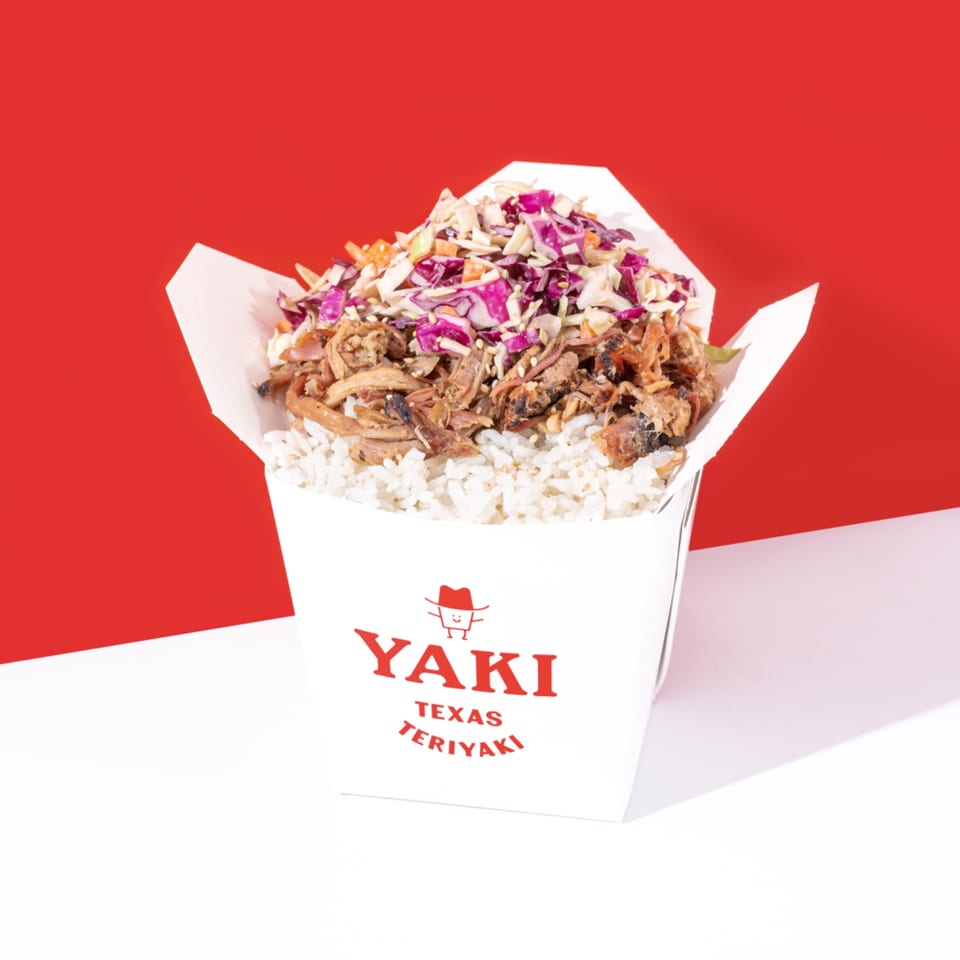Yaki Texas Teriyaki branded takeout box filled with white rice, shredded meat, and colorful coleslaw.