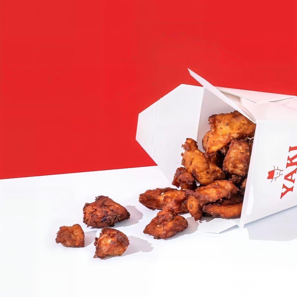 Crispy Yaki Texas Teriyaki chicken pieces spilling from a white takeout box against a red background.