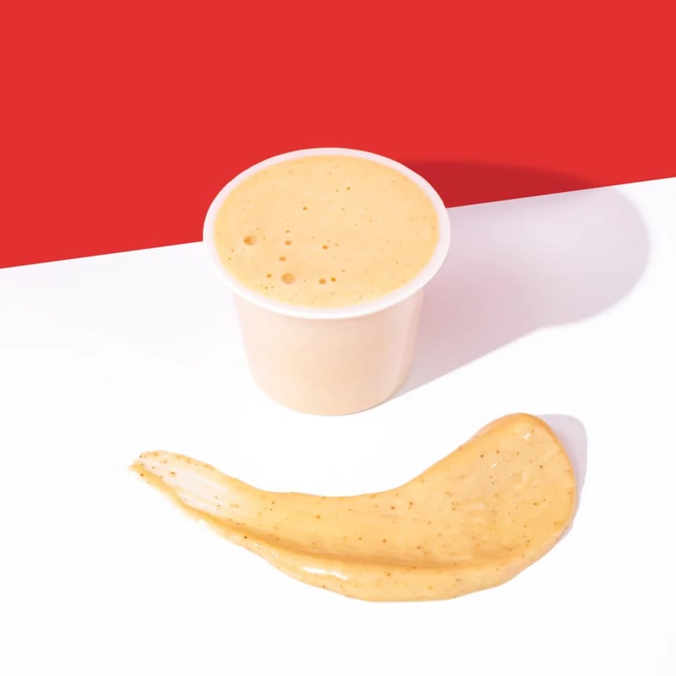 A small cup of Yaki Texas Teriyaki sauce and a smear of the sauce on a white and red background.