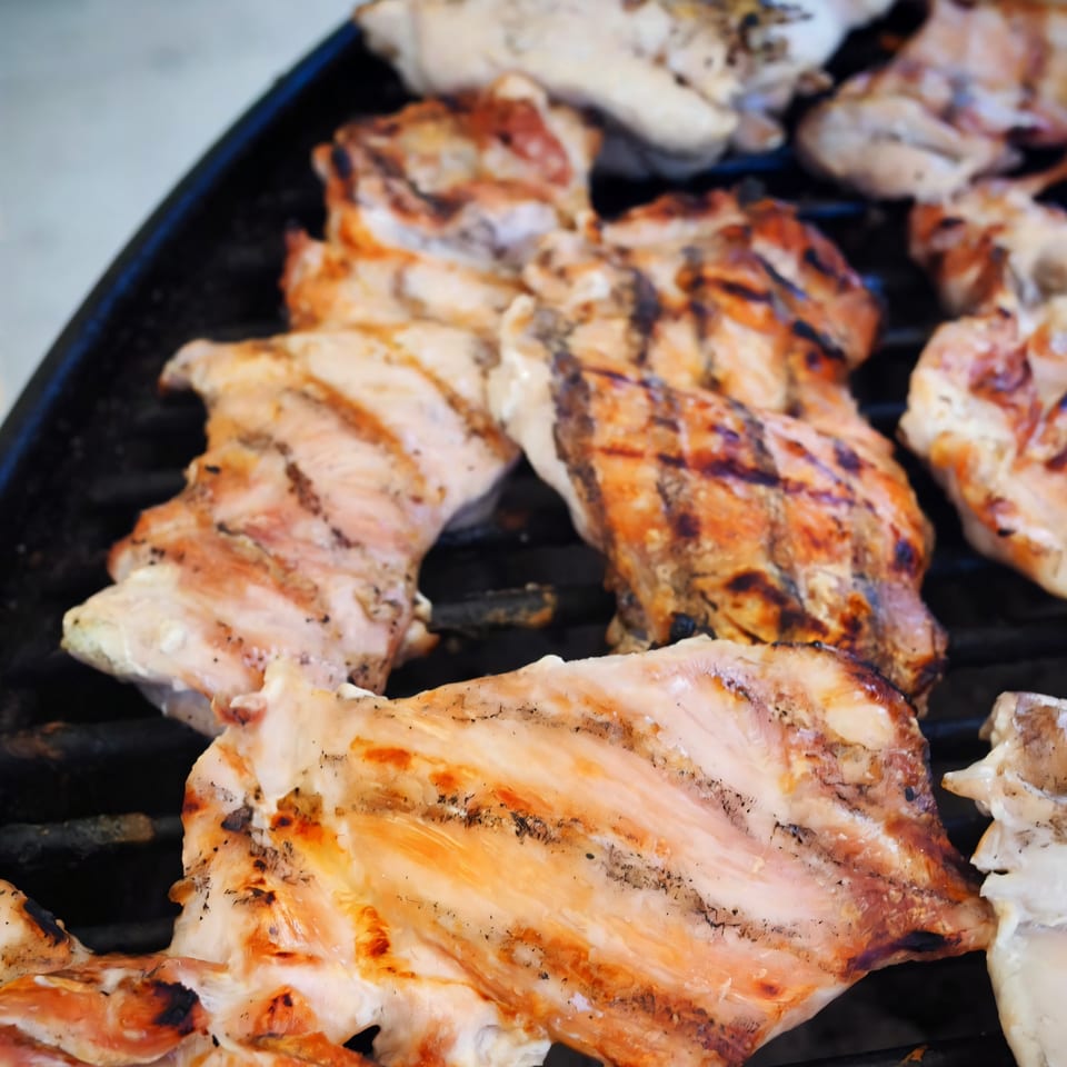 Grilled chicken pieces with char marks cooking on a black barbecue grate, ready for Yaki Texas Teriyaki.